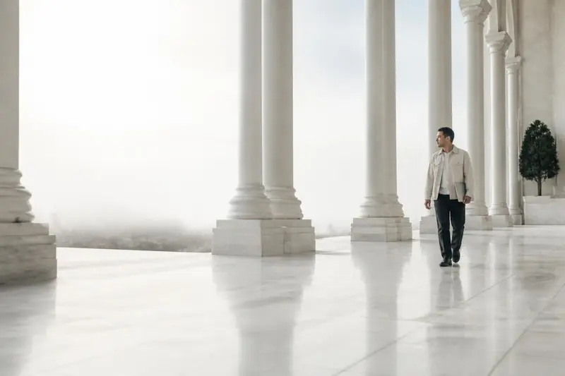 A founder walking through a sunlit colonnade of pale stone